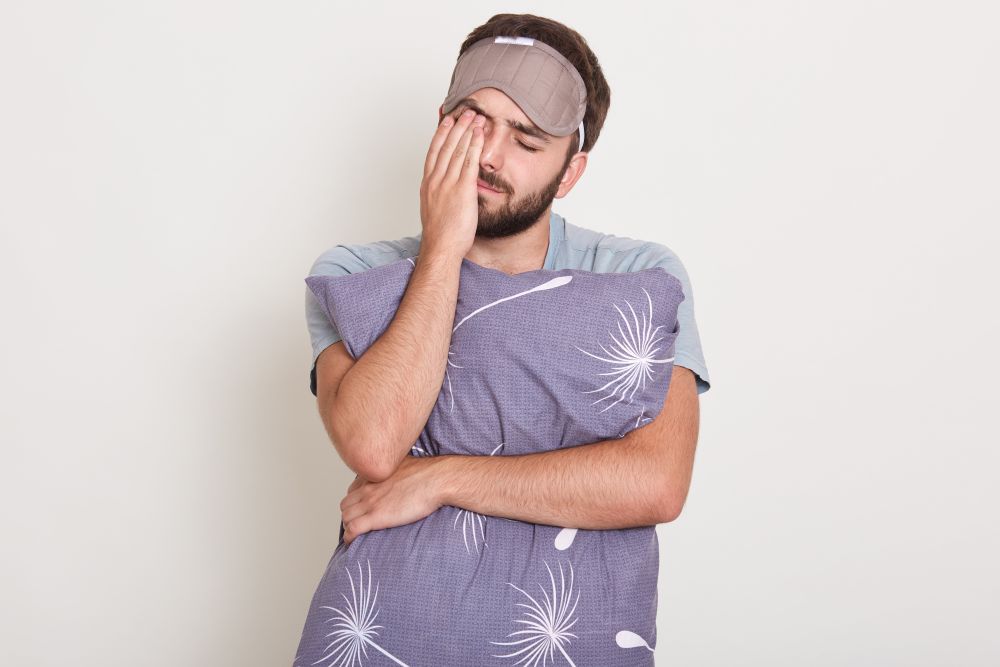 How to Avoid Teeth Grinding While Sleeping 2 indoor shot young attractive man waking morning wants sleep handsome guy stretching yawning holding his pillos October 2025 Vadodara India