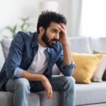 male depression concept upset young indian man sitting couch home January 2026 Vadodara India